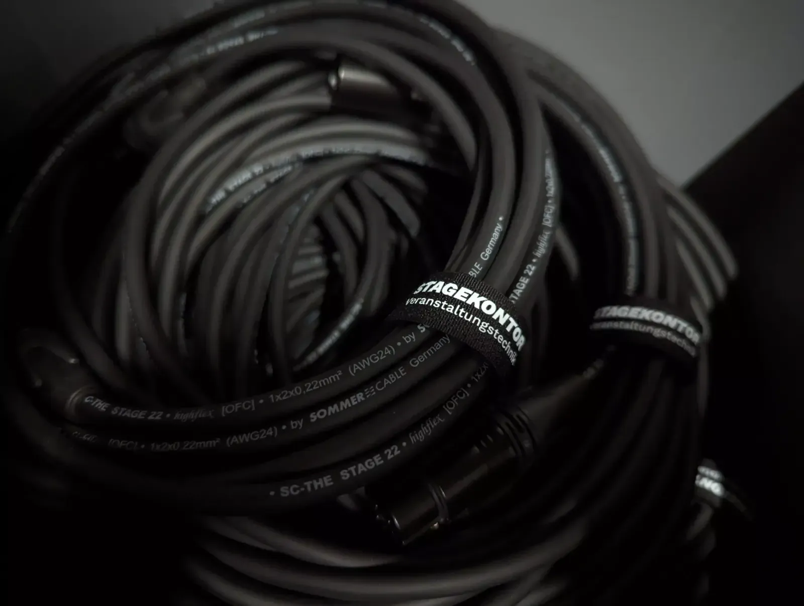 Aufgerollte schwarze Kabel mit Klettbindern, auf denen „STAGEKONTOR Veranstaltungstechnik“ steht