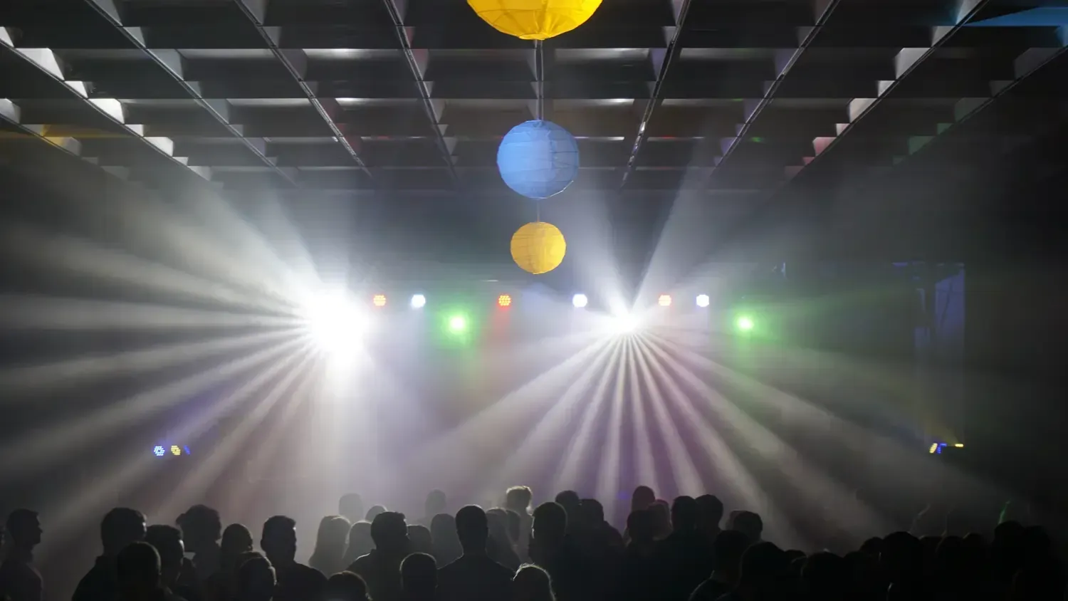 Lichtstrahlen von Moving Heads im Nebel über einer tanzenden Menge