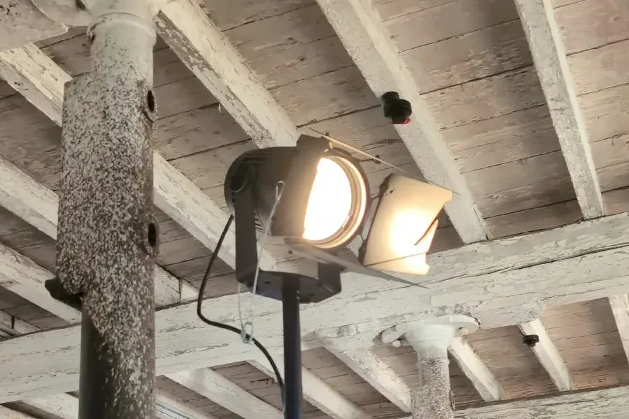 Stufenlinsen-Scheinwerfer mit Torblende auf einem Stativ unter einer alten Holzdecke